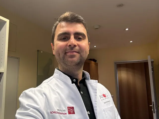Dr. Mehmet Kaymakoğlu beyaz önlüğüyle muayene odasında gülümserken